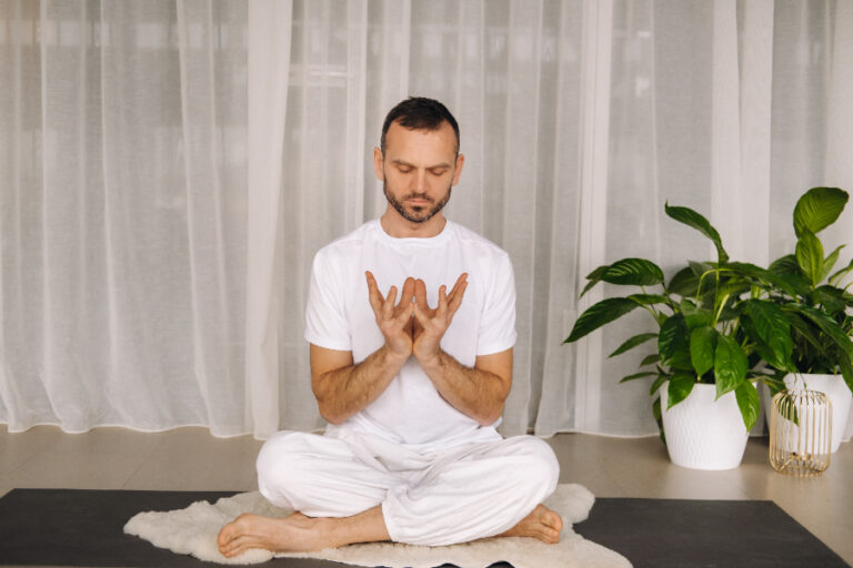 Un homme habillé en blanc et assis sur un tapis en faisant de la méditation spirituelle