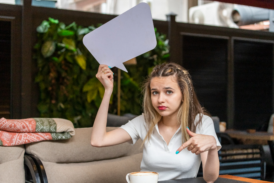 Une jeune fille qui n'a aucune conversation dans une cafétéria, et tient un icône de bulle de conversation vide