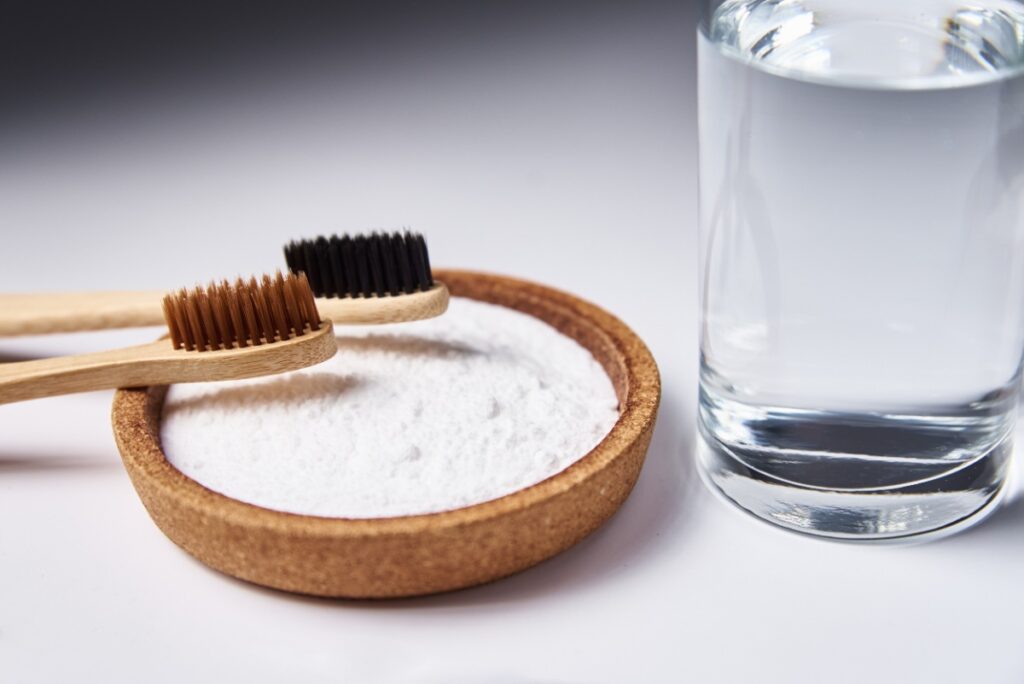 Deux brosses à dents sur une bicarbonate de soude placés à côté d'un verre d'eau