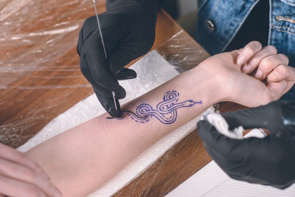 Un professionnel portant un gant et réalise un tatouage de dragon japonais sur le bras d'une personne