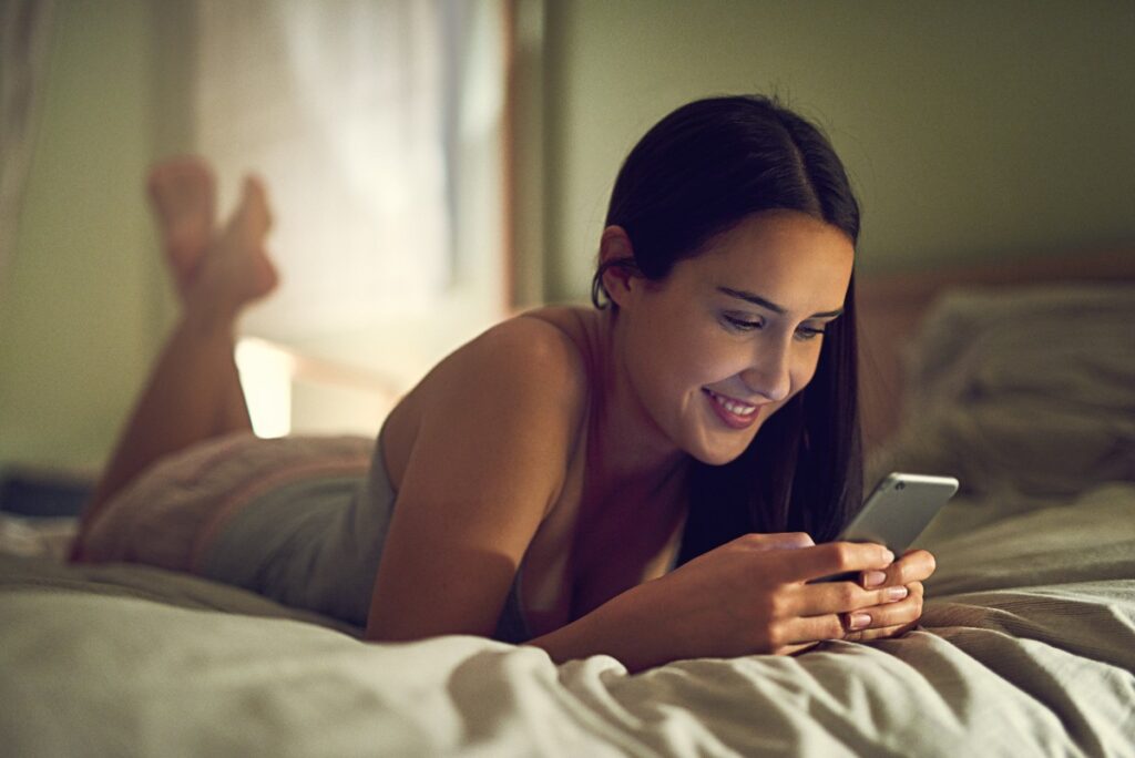 Une femme souriante allongée au lit avec son téléphone