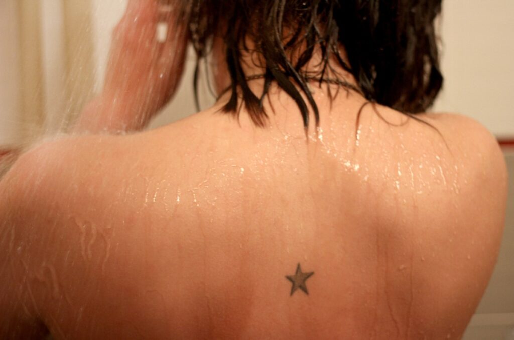 Une femme dans la douche avec des cheveux mouillés et un tatouage sur le dos
