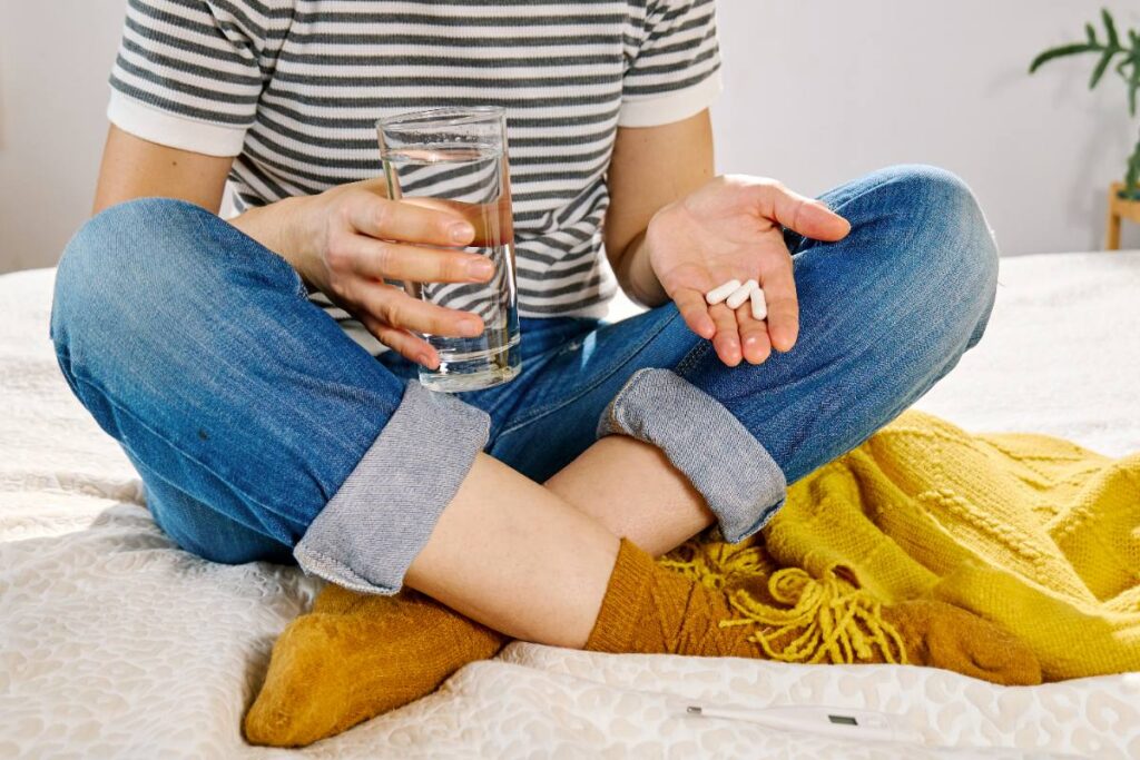 Une femme assise sur le lit avec des pilules et un verre d'eau