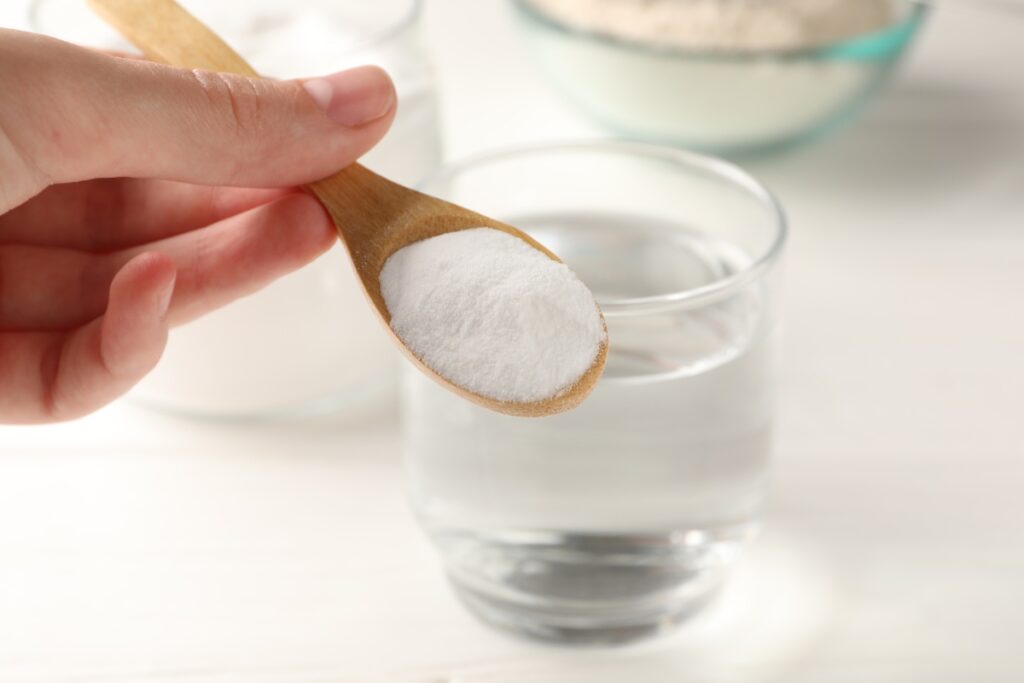 Une personne tenant une cuillère de bicarbonate de soude près d'un verre d'eau